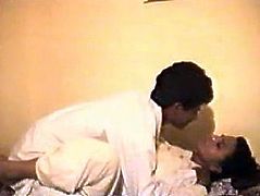 This couple is fornicating in a hotel room. They both are wearing white robes pleasing one another on a bed. The guy enjoys kneading big saggy boobs of his lover.