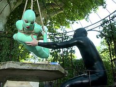 Extremely spoiled babe in latex outfit hangs suspended by ropes in the garden terrace over a table and she is completely at the mercy of her cruel mistress. This hot dominatrix in latex outfit fucks her slave's mouth with her strap-on dildo.