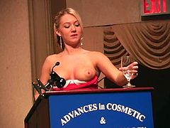 Charming blonde babe in a red dress lifts a dress up to show her hot ass in a conference hall. She also rehearses her speech and masturbates on the stage.