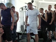 A tied up guy sucks huge dicks and get toyed in a gym